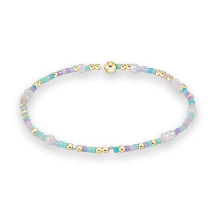 Beaded jewelry stretch bracelet on a white background featuring a colorful sequence of pastel mint, lavender, and light blue seed beads accented with polished gold metallic spheres and white faux pearls