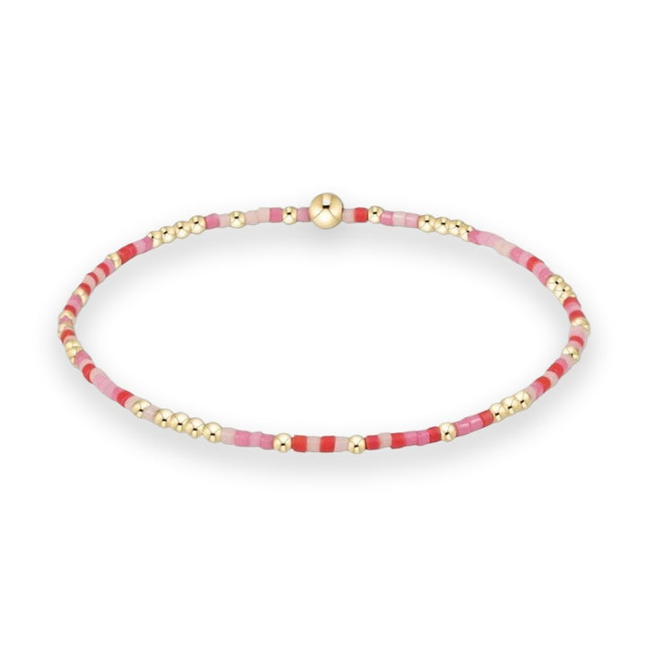 Beaded jewelry bracelet centered against a white background featuring an alternating pattern of vibrant red, soft pink, and magenta seed beads accented by small polished gold spheres and a single larger gold accent bead