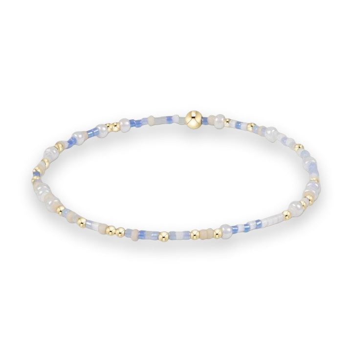Handcrafted beaded jewelry bracelet on a white background featuring a sequence of light blue and white seed beads accented with polished gold-tone spheres and a central larger gold bead