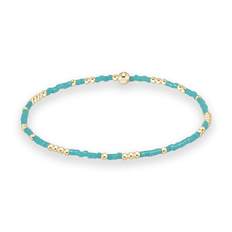 Beaded jewelry stretch bracelet displayed on a white background featuring vibrant turquoise cylinder beads alternating with polished gold spheres and a large central gold bead