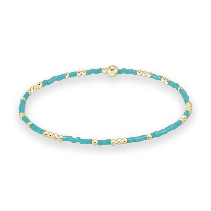 Beaded jewelry stretch bracelet displayed on a white background featuring vibrant turquoise cylinder beads alternating with polished gold spheres and a large central gold bead