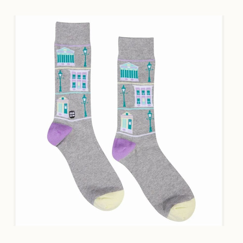 Knit socks by The Bath Sock Company featuring an illustrated pattern of Bath England landmarks including the Roman Baths and Georgian townhouses with teal lamp posts purple heels and yellow toes