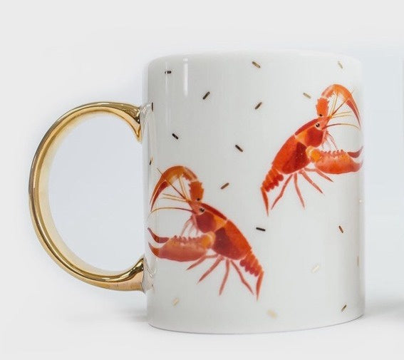 Ceramic mug by Yvonne Ellen featuring two vibrant red-orange lobster illustrations on a white surface with a polished gold-gilded handle and scattered metallic gold dash accents