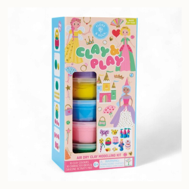 Product photography of a Floss & Rock Clay & Play air dry clay modelling kit featuring whimsical princesses and a colorful fairytale castle alongside stacked tubs of vibrant pink and yellow clay on a white background
