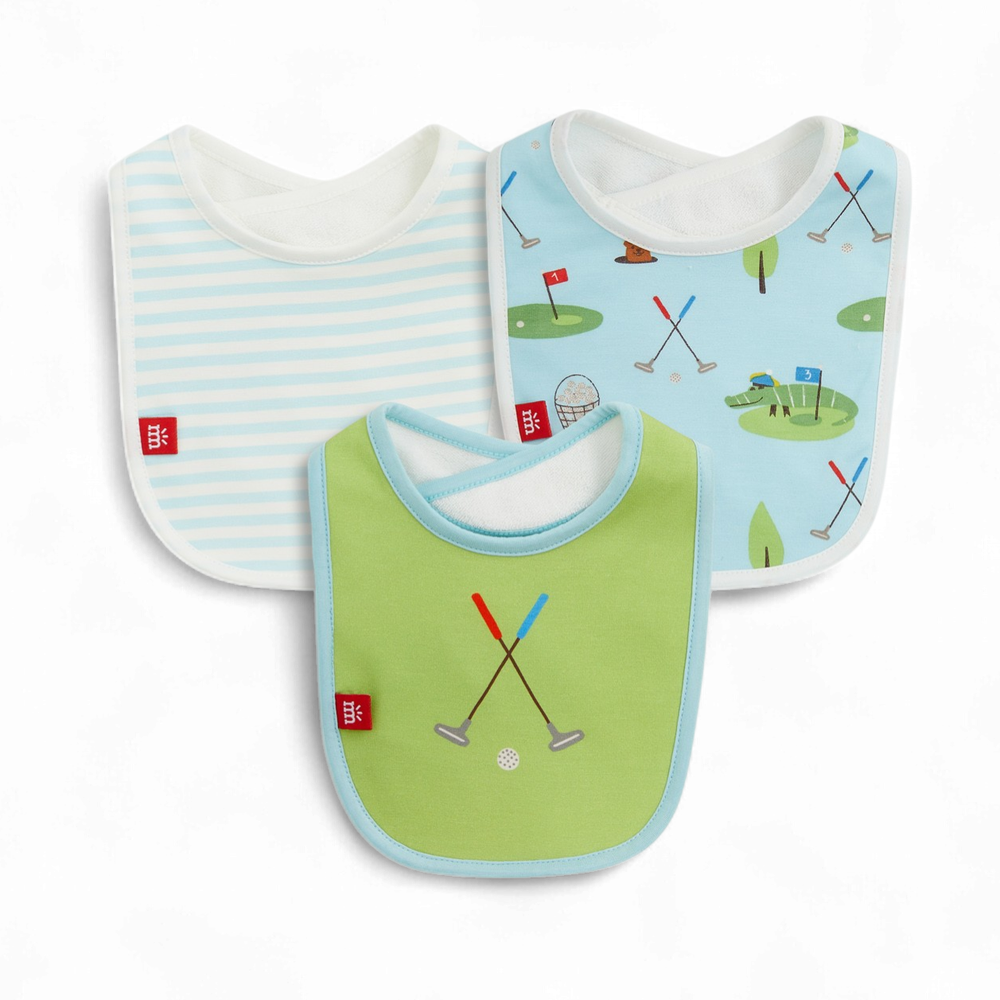 Product photography by Mothercare showcasing three baby bibs on a white background including a light blue striped design, a solid green bib with crossed golf clubs, and a patterned blue bib featuring a golfing alligator and small red flags