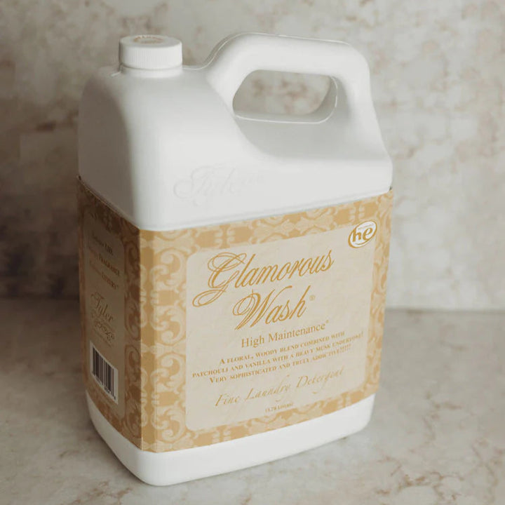 Product photograph of Tyler Candle Company Glamorous Wash High Maintenance laundry detergent on a marble countertop featuring an ornate gold damask label, cursive typography, and an embossed logo on the white plastic jug