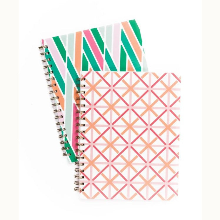 Product photography of two spiral-bound notebooks on a white background featuring a vibrant green and pink diagonal stripe pattern and a warm pink and orange geometric lattice design with metallic gold coils