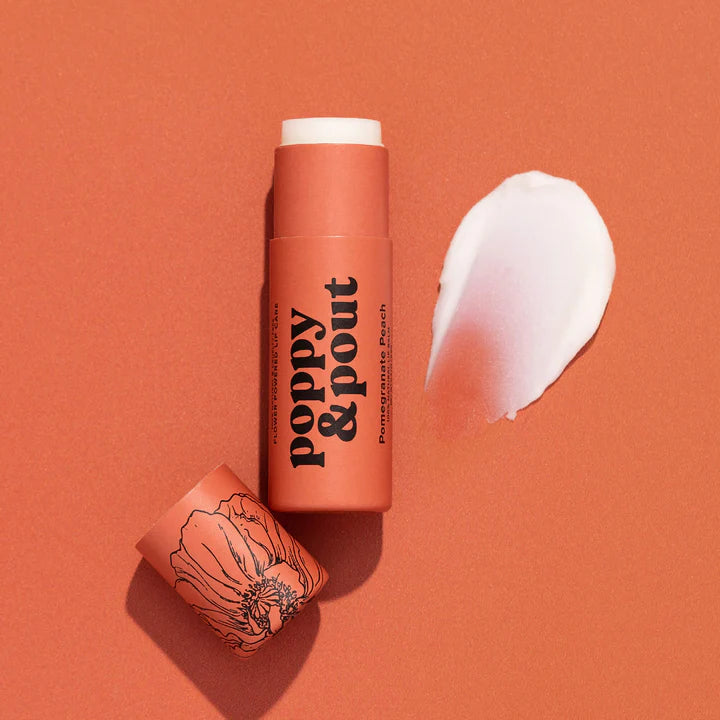 Studio photograph by Poppy &amp; Pout featuring a Pomegranate Peach lip balm on a monochromatic peach background with a creamy white product smear and a black line-art poppy illustration on the cap