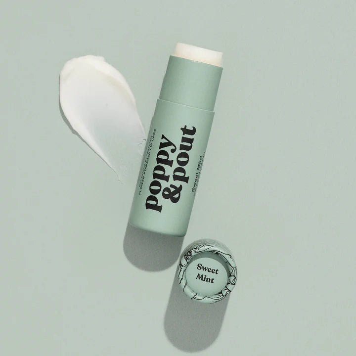Commercial photograph by Poppy &amp; Pout of Sweet Mint lip balm on a sage green studio background, featuring the brand logo, a textured white cream swipe, and a matte cardboard tube with a floral-illustrated lid