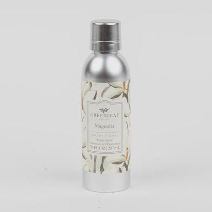 Studio photograph of a Greenleaf Magnolia room spray bottle on a plain white background featuring a sleek silver aluminum finish, elegant cream floral illustrations, and a metallic screw cap