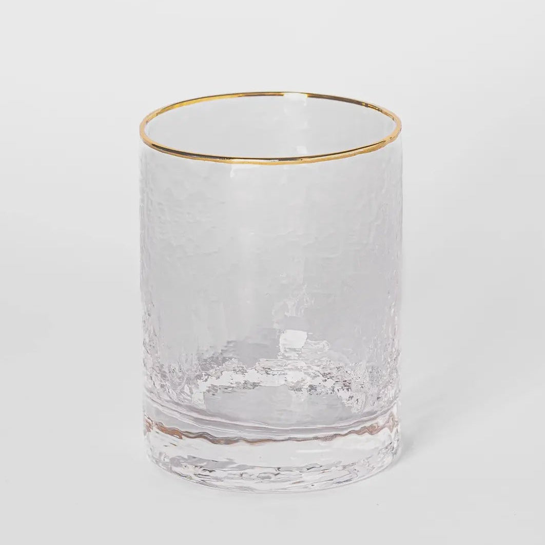 Hammered glass tumbler featuring a thin metallic gold rim and a textured clear surface set against a minimal white background with a thick weighted base
