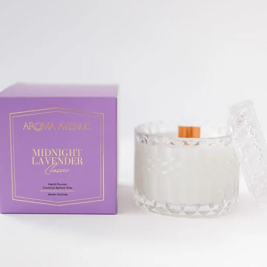 Product photograph by Aroma Avenue of a Midnight Lavender candle featuring a wooden wick in a diamond-patterned clear glass jar next to a purple box with gold foil lettering on a white surface