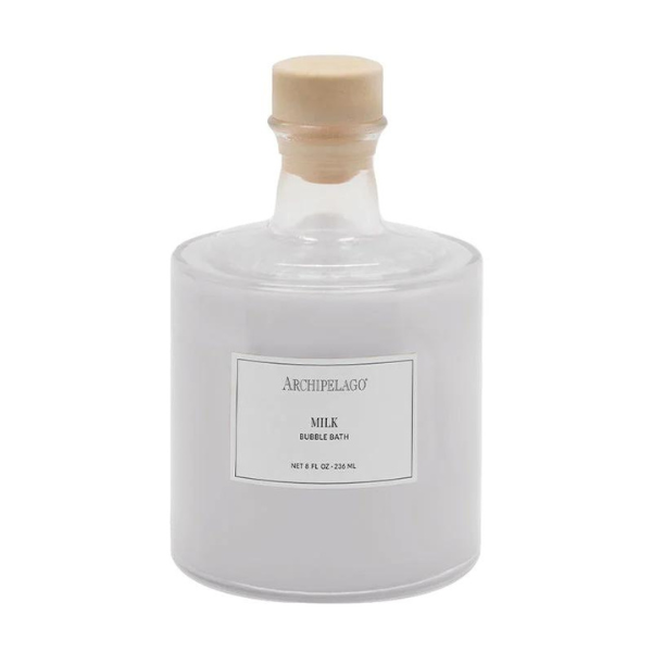 Product photography by Archipelago of a Milk Bubble Bath bottle on a white background featuring a frosted glass vessel, a rustic wooden stopper, and the iconic Archipelago brand label