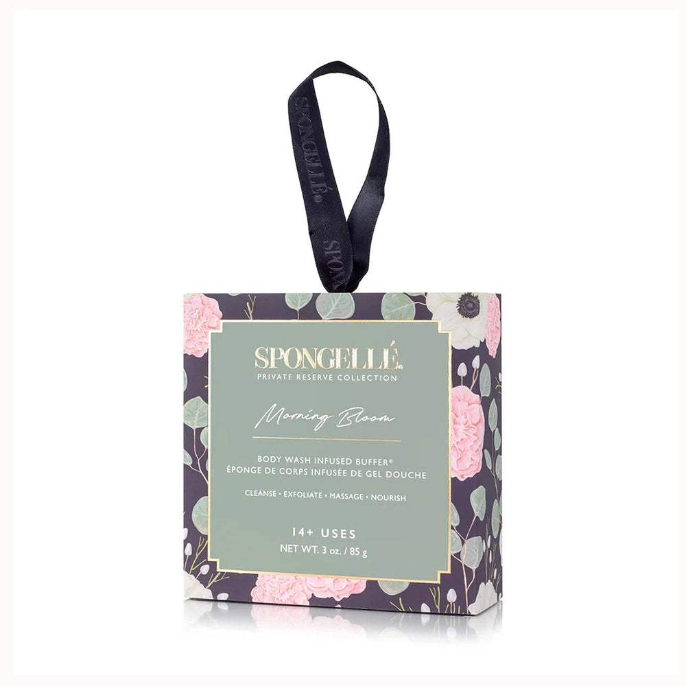 Product photography of Spongellé Morning Bloom Body Wash Infused Buffer packaging showcasing a dark floral pattern of pink peonies and green eucalyptus leaves with a gold-trimmed sage label and a black branded ribbon handle