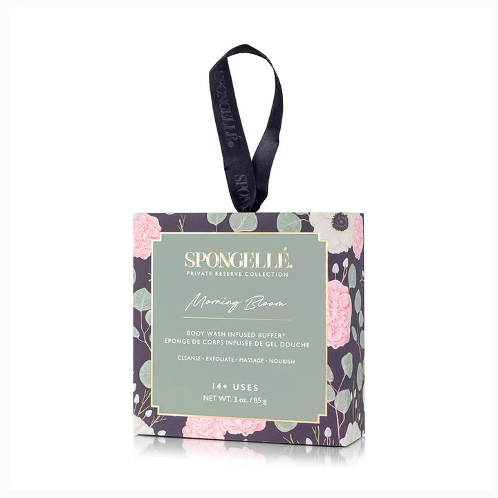 Product photography of Spongellé Morning Bloom Body Wash Infused Buffer packaging showcasing a dark floral pattern of pink peonies and green eucalyptus leaves with a gold-trimmed sage label and a black branded ribbon handle
