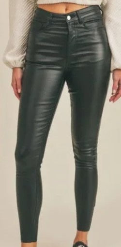 Studio photograph of high-waisted black coated skinny pants with a glossy finish and single silver button paired with a textured cream sweater against a neutral studio background