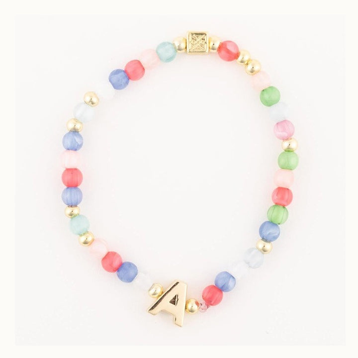 Handcrafted beaded jewelry piece featuring a colorful initial bracelet on a white background with a gold-tone letter A charm, multi-colored cat-eye beads, and a square metal logo bead