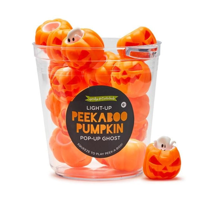 Commercial product photograph by Upcakes & Cartwheels of a clear bucket filled with orange Light-Up Peekaboo Pumpkin toys featuring pop-up white ghosts and carved jack-o'-lantern faces on a white background