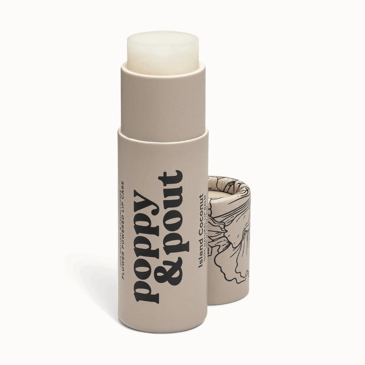 Product photograph by Poppy &amp; Pout of an Island Coconut lip balm tube on a black background featuring a tan cardboard container with bold black serif typography and an intricate floral line drawing on the cap
