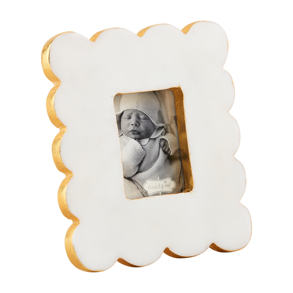 White marble and gold leaf scalloped picture frame by Mud Pie displaying a black and white baby photograph with shimmering gilded edges and a textured wavy border against a neutral white backdrop