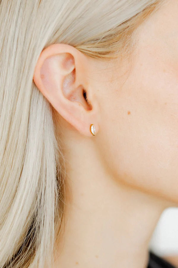 Photograph of a gold marquise-cut diamond stud earring on a woman's earlobe featuring long platinum blonde hair and a tiny beauty mark on her cheek