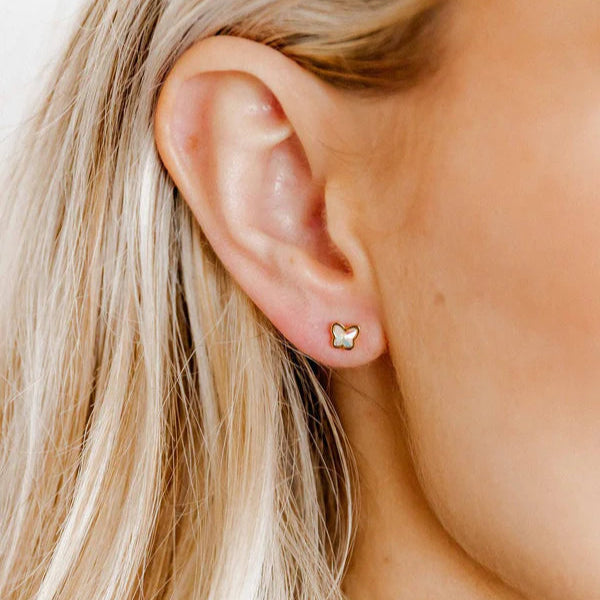 Digital photograph of a gold butterfly stud earring with an iridescent mother-of-pearl inlay worn on a human ear lobe and framed by strands of light blonde hair