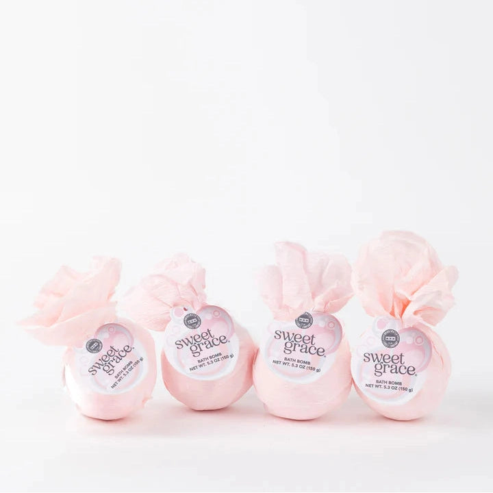 Product photography by Bridgewater Candle Company of four Sweet Grace bath bombs on a minimalist white background featuring delicate pink tissue paper wrapping with decorative ruffled tops and circular labels