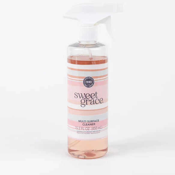 Studio photograph of Bridgewater Candle Company Sweet Grace Multi Surface Cleaner on a white background featuring a clear bottle filled with pinkish liquid and a white trigger spray nozzle above a pink and gray striped label