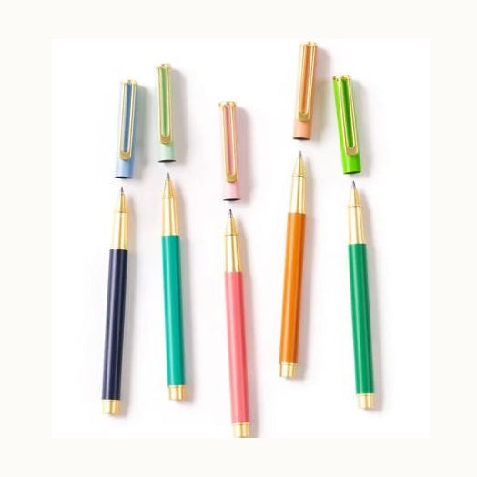 Product photograph of Ferris Wheel Press rollerball pens on a white background featuring gold-plated U-shaped clips and vibrant barrels in navy blue, coral pink, and mint green