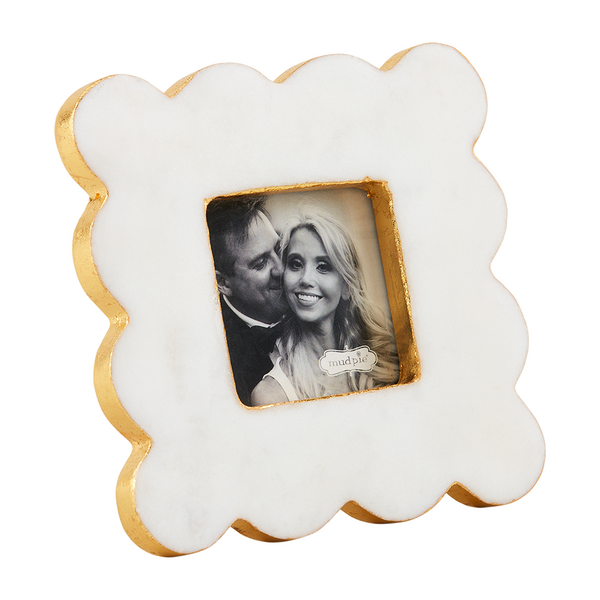 Marble and gold-leaf picture frame by Mud Pie featuring a black and white portrait of a smiling couple within a square window accented by scalloped edges and a metallic gold finish against a plain white backdrop