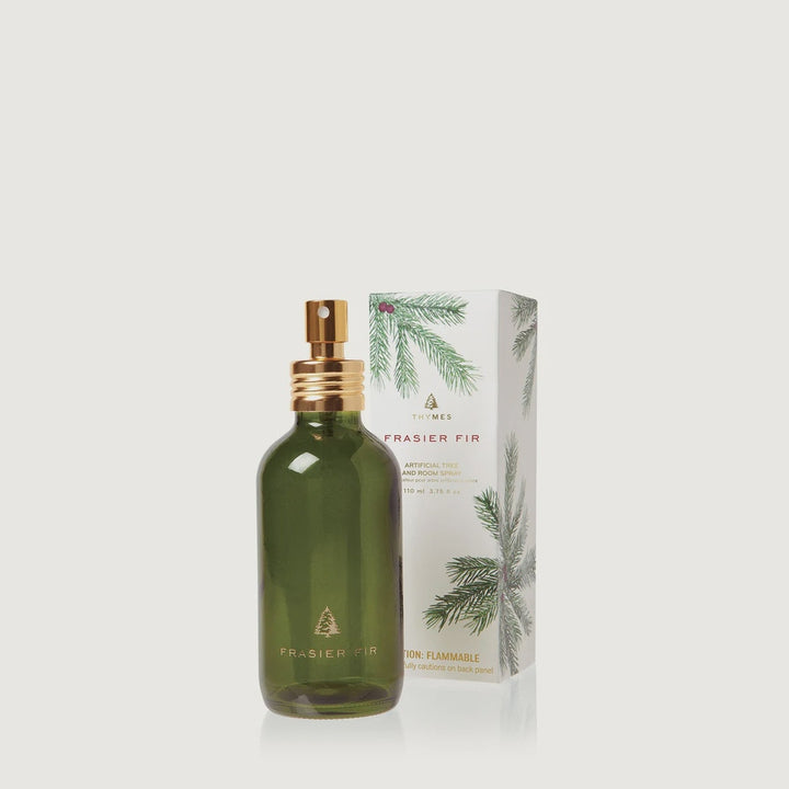 Product photograph of Thymes Frasier Fir room spray featuring a forest green glass bottle with a gold-tone pump and a decorative white box illustrated with green pine needles