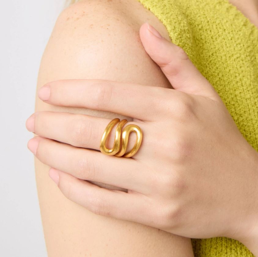 Jewelry photograph of a matte gold sculptural triple-band ring on a model's hand resting against her shoulder paired with a vibrant lime green textured knit top