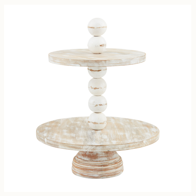 Hand-carved wood two-tier serving stand with a distressed whitewash finish featuring a central pillar of five stacked wooden orbs and a wide round pedestal base on a white background