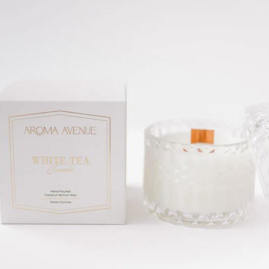 Studio product photograph by Aroma Avenue of a White Tea scented candle and its minimalist box in a bright studio setting featuring a diamond-textured glass jar with a wide wooden wick and elegant gold foil lettering