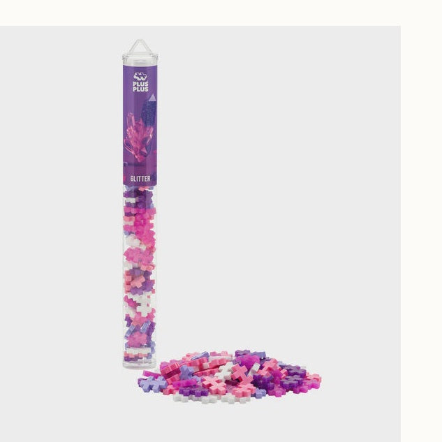 Plastic interlocking building toy by Plus-Plus featuring the Glitter mix construction set in a clear storage tube and scattered on a neutral background with the brand logo and shimmering translucent pink deep purple and white cross-shaped pieces