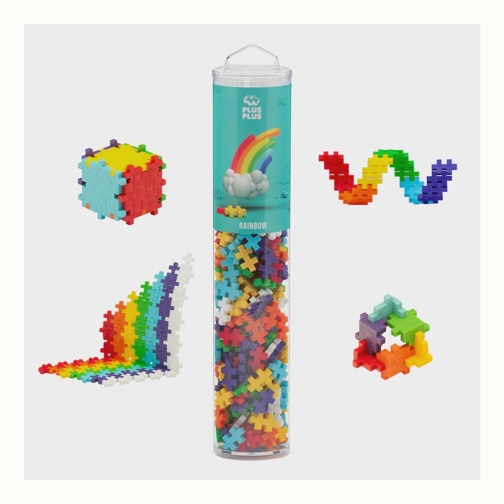 Plus-Plus construction toy set featuring a clear Rainbow tube filled with multi-colored interlocking pieces alongside a vibrant geometric cube and a tiered staircase model on a neutral background