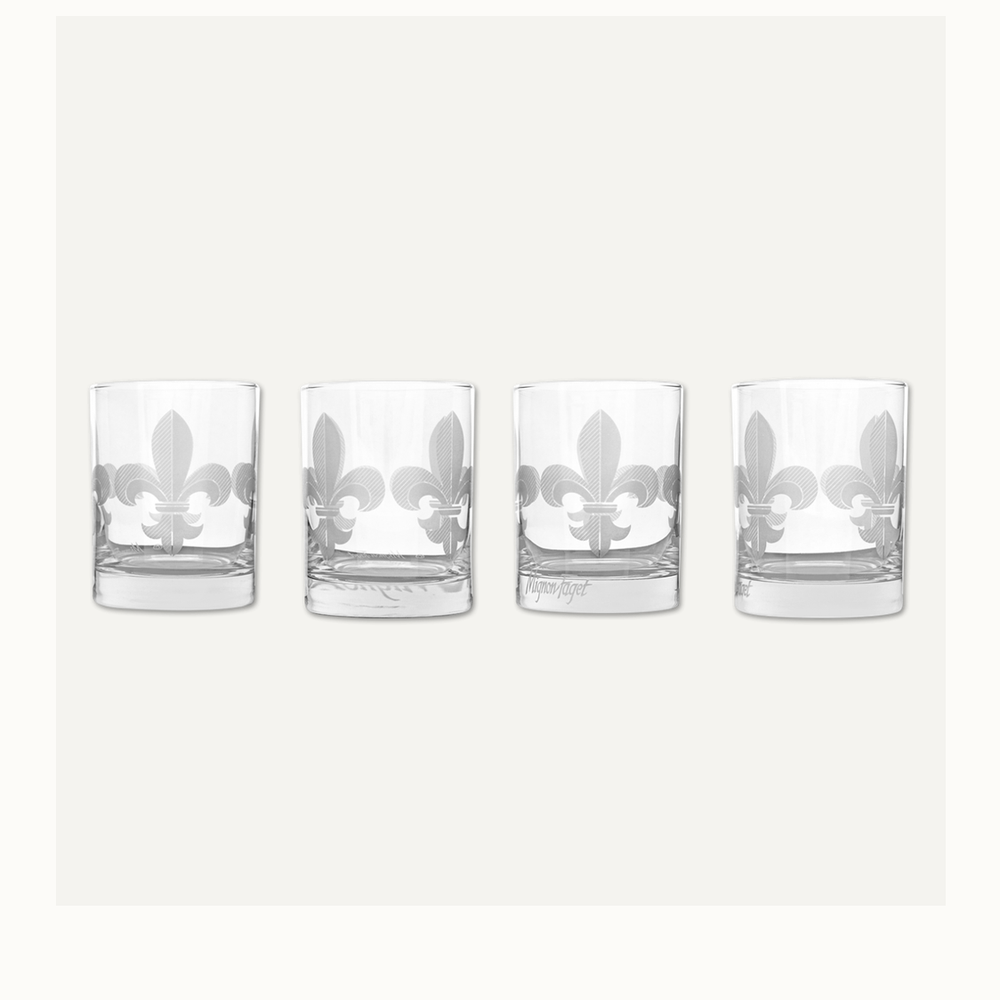 Etched glassware by Mignon Faget featuring a set of four rocks glasses against a neutral background showcasing the iconic New Orleans fleur-de-lis with a frosted cross-hatched pattern and heavy weighted bases