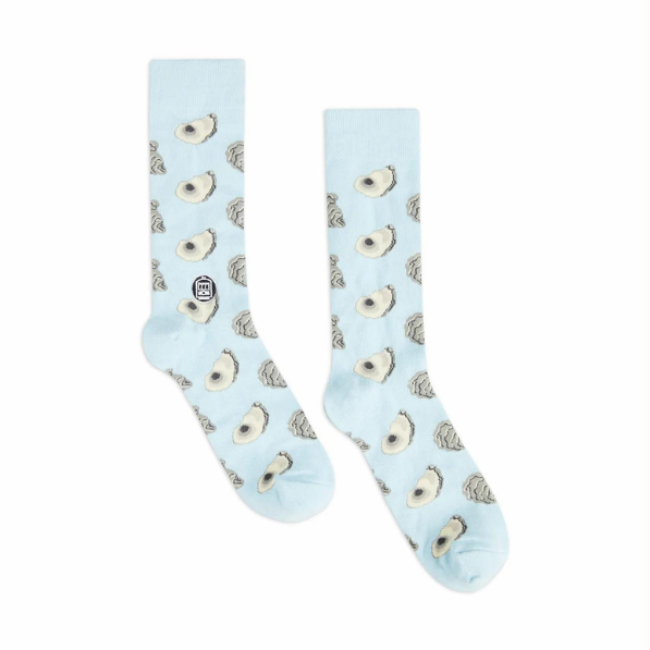 Cotton blend crew socks by Dirty Coast featuring a repeating pattern of grey and cream oyster shells on light blue fabric with a New Orleans streetcar logo on a white background