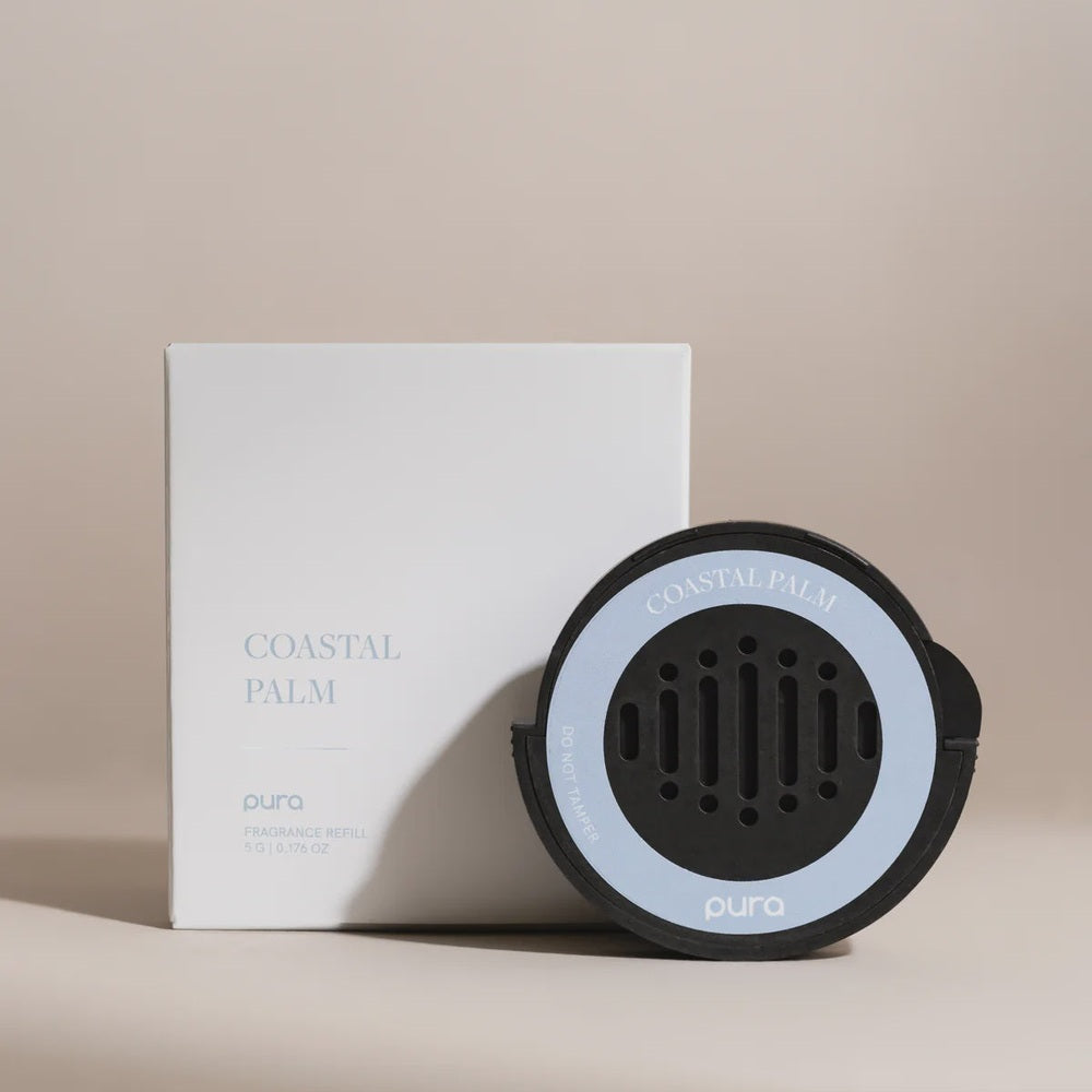 Product photography by Pura of a Coastal Palm fragrance refill and white packaging box on a neutral beige background featuring a light blue circular label on the vented black pod and minimalist sans-serif branding