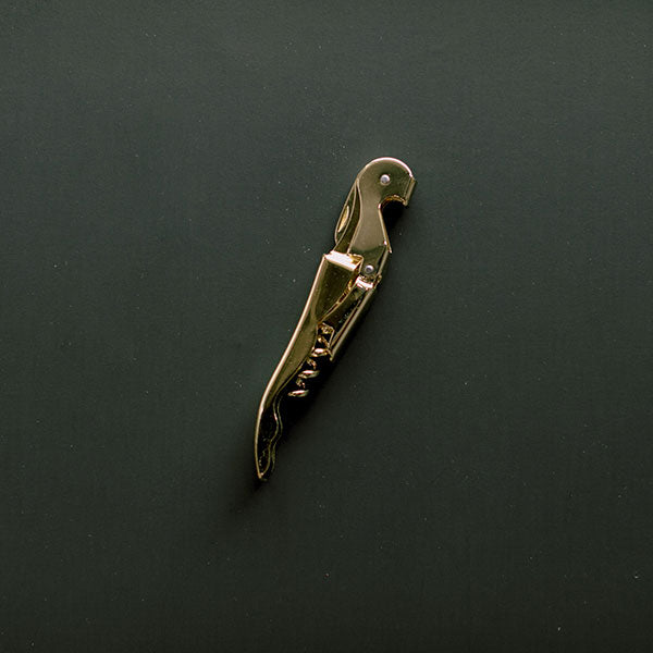 Gold-plated zamak sommelier corkscrew by Alessandro Mendini for Alessi featuring a sleek parrot-shaped silhouette with a reflective metallic finish and integrated spiral on a dark matte background