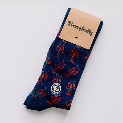 Bonfolk cotton crew socks from New Orleans featuring a repeated red crawfish pattern and an embroidered St. Charles streetcar emblem on navy blue fabric with a brown branded tag