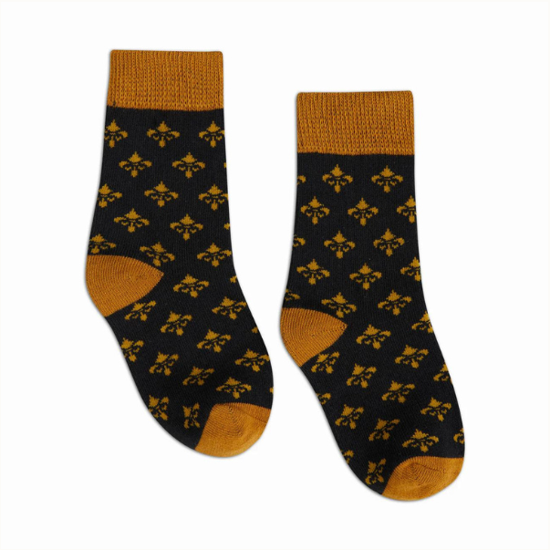 Knit socks featuring a repeating mustard yellow fleur-de-lis pattern on a black background with matching ribbed cuffs and reinforced heels against a white studio background