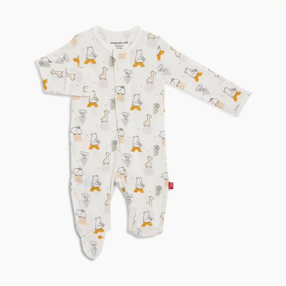 Product photograph by Magnetic Me of a white newborn baby footie featuring a whimsical print of hand-drawn giraffes and bears accented by mustard yellow triangles and lavender circles on a white studio background