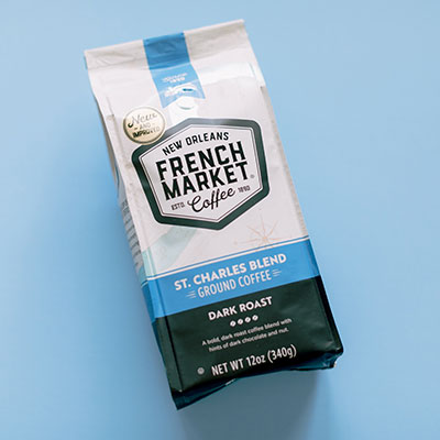 Product photograph of French Market Coffee showcasing a bag of St. Charles Blend from New Orleans on a light blue backdrop featuring a gold New and Improved seal and a dark green panel for the dark roast ground coffee