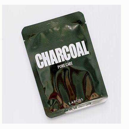 Commercial product photograph by LAPCOS showcasing a charcoal pore care sheet mask packet on a white background with bold white typography, a glossy dark green reflective finish, and a silver-sealed bottom edge showing an expiration stamp