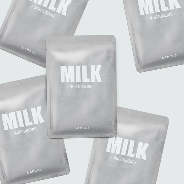 Studio product photograph by LAPCOS of Milk Moisturizing sheet mask packets arranged on a neutral grey background with reflective silver foil and bold white block typography