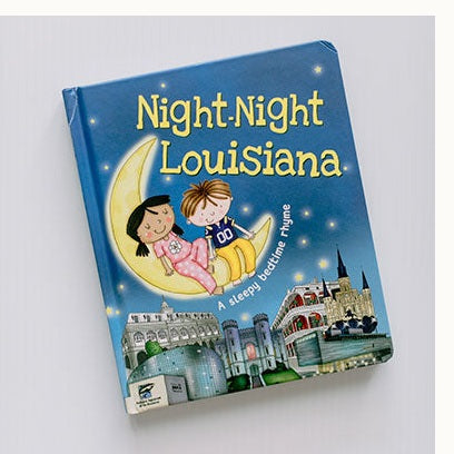Illustrated board book cover by Katherine Sully and Helen Turner for Night-Night Louisiana featuring two children on a yellow crescent moon above the St. Louis Cathedral and Audubon Aquarium with a girl in pink floral pajamas and a boy in a purple football jersey