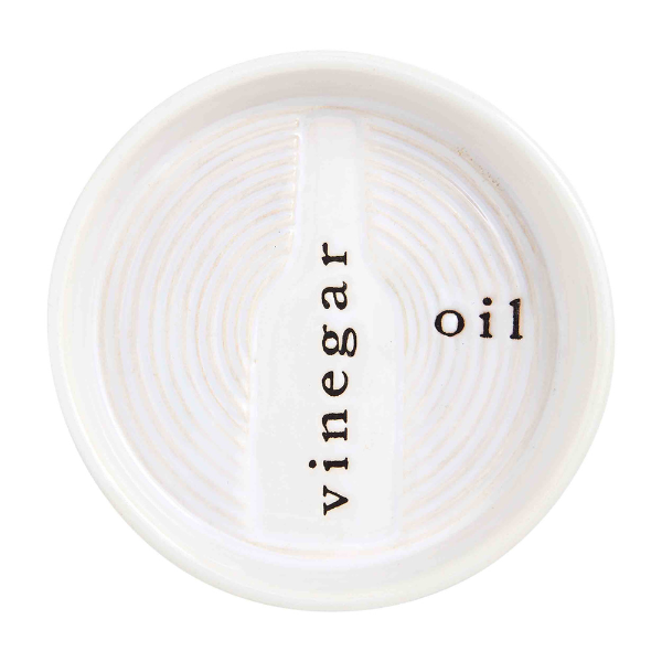 Ceramic stoneware dipping dish by Mud Pie featuring a circular bread plate with a debossed central bottle silhouette labeled vinegar and oil in black typewriter font surrounded by concentric white-glazed ridges