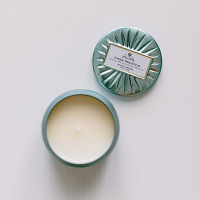 Product photography by Voluspa of a Casa Pacifica scented candle on a white background featuring a metallic seafoam green tin with a decorative embossed sunburst lid and creamy white wax