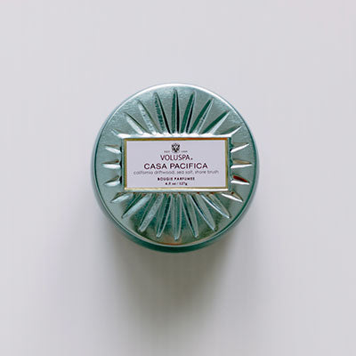 Product photograph of a Voluspa Casa Pacifica scented candle lid featuring a metallic seafoam green finish with an embossed sunburst pattern and a central white label with gold trim